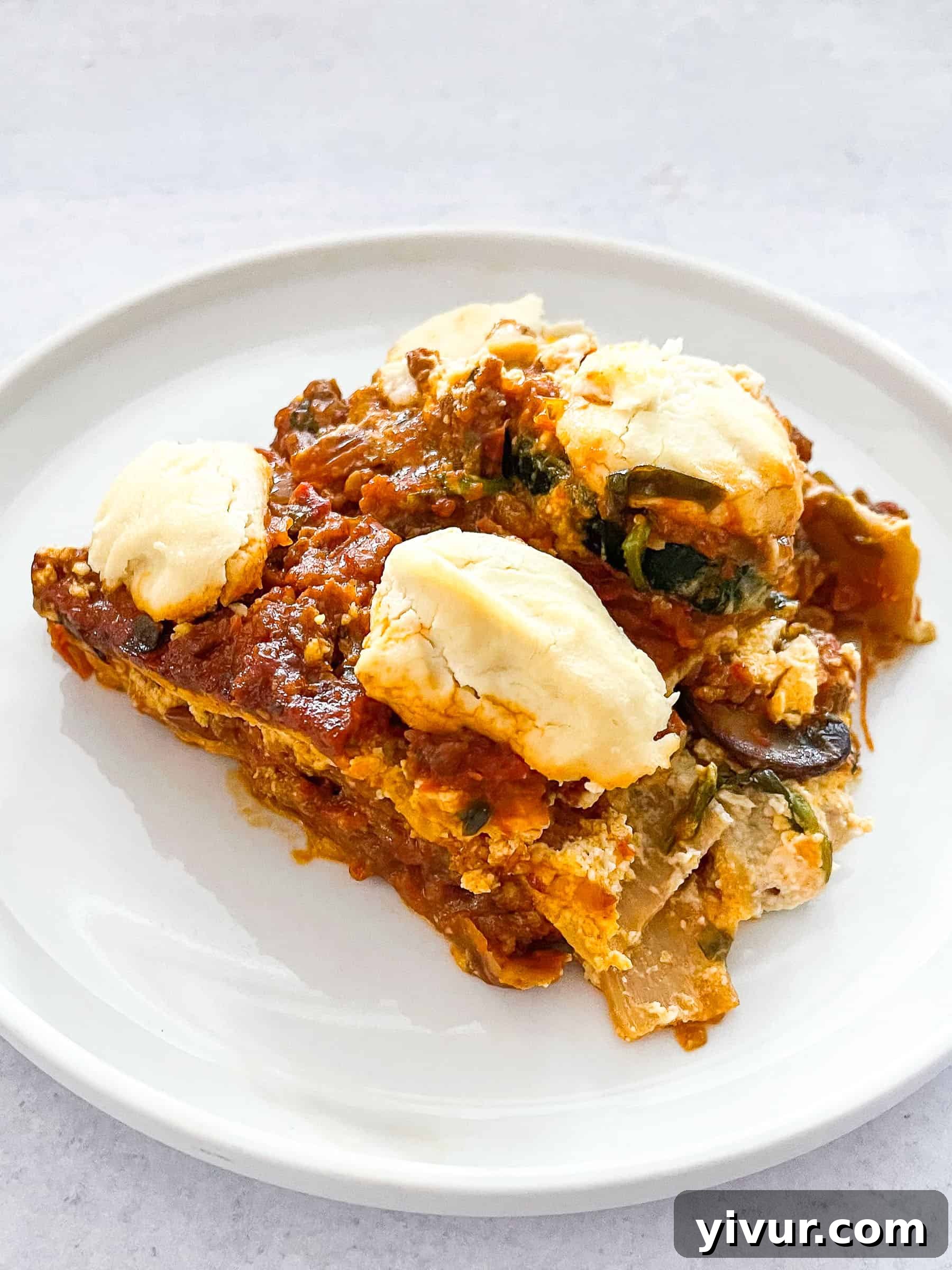 Dairy-free keto lasagna generously topped with creamy dairy-free ricotta cheese, served on a pristine white plate against a clean white background.