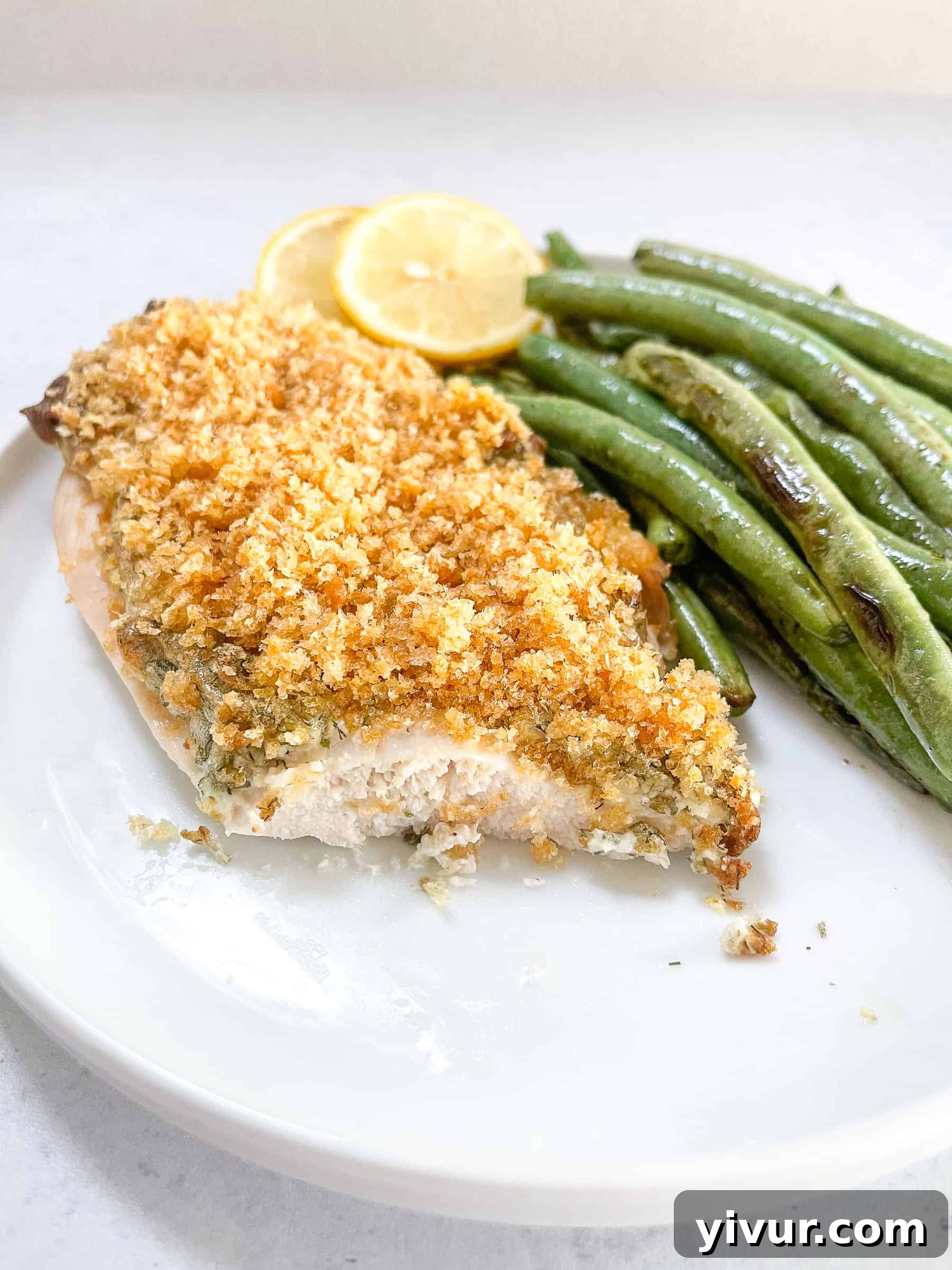 A close-up of a serving of Keto Crispy Ranch Chicken, garnished with fresh lemon and green beans, on a white plate with a clean backdrop.