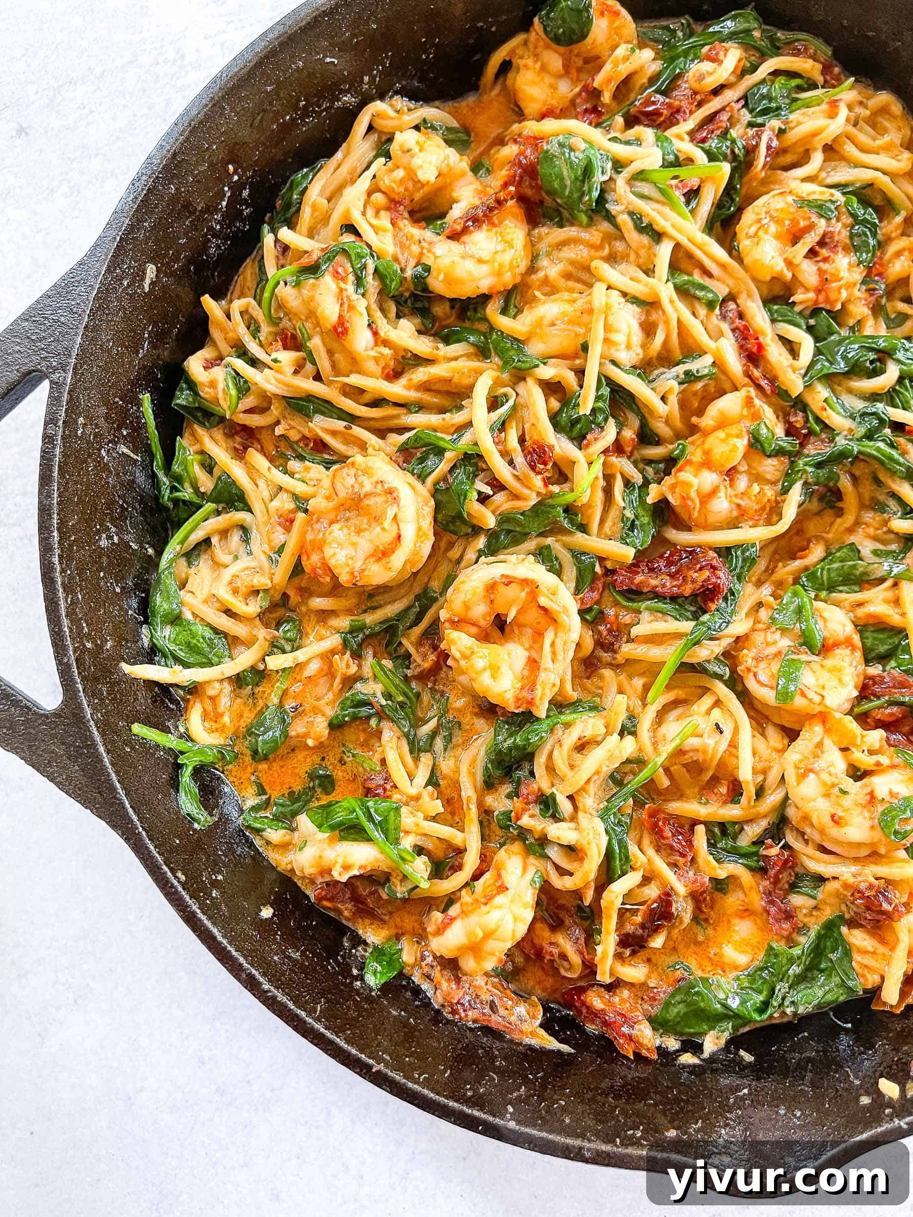 Keto Creamy Tuscan Shrimp Pasta topped with basil in a cast iron skillet with a white background
