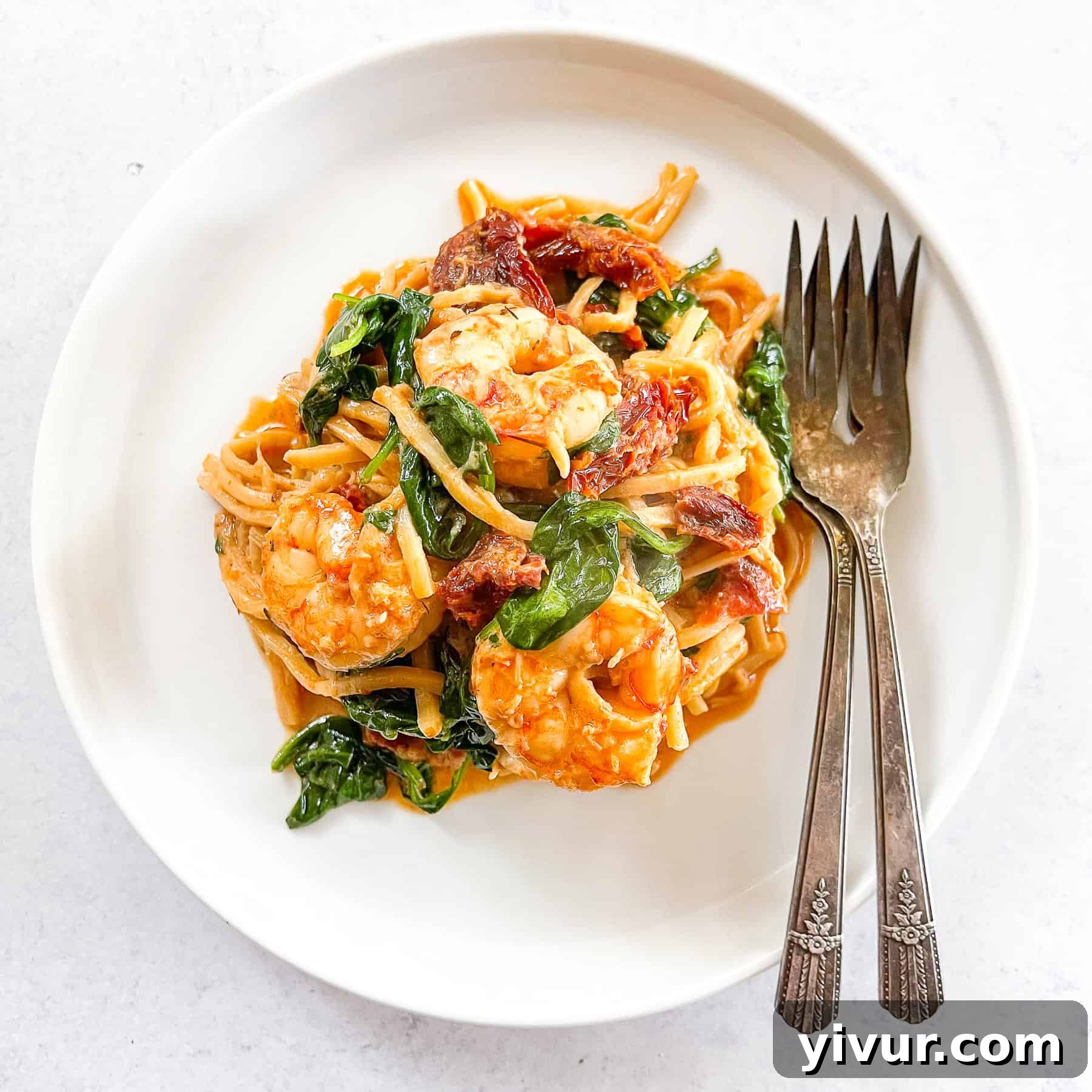 Keto Creamy Tuscan Shrimp Pasta topped with basil on a white plate with two forks and a white background