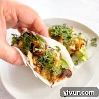 a hand holding a shredded chicken taco in a jicama tortilla wrap