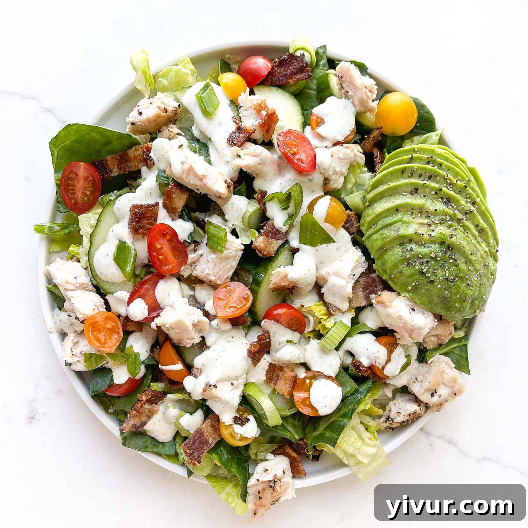 A refreshing salad topped with ranch dressing, grilled chicken, avocado, tomatoes, and crispy bacon.