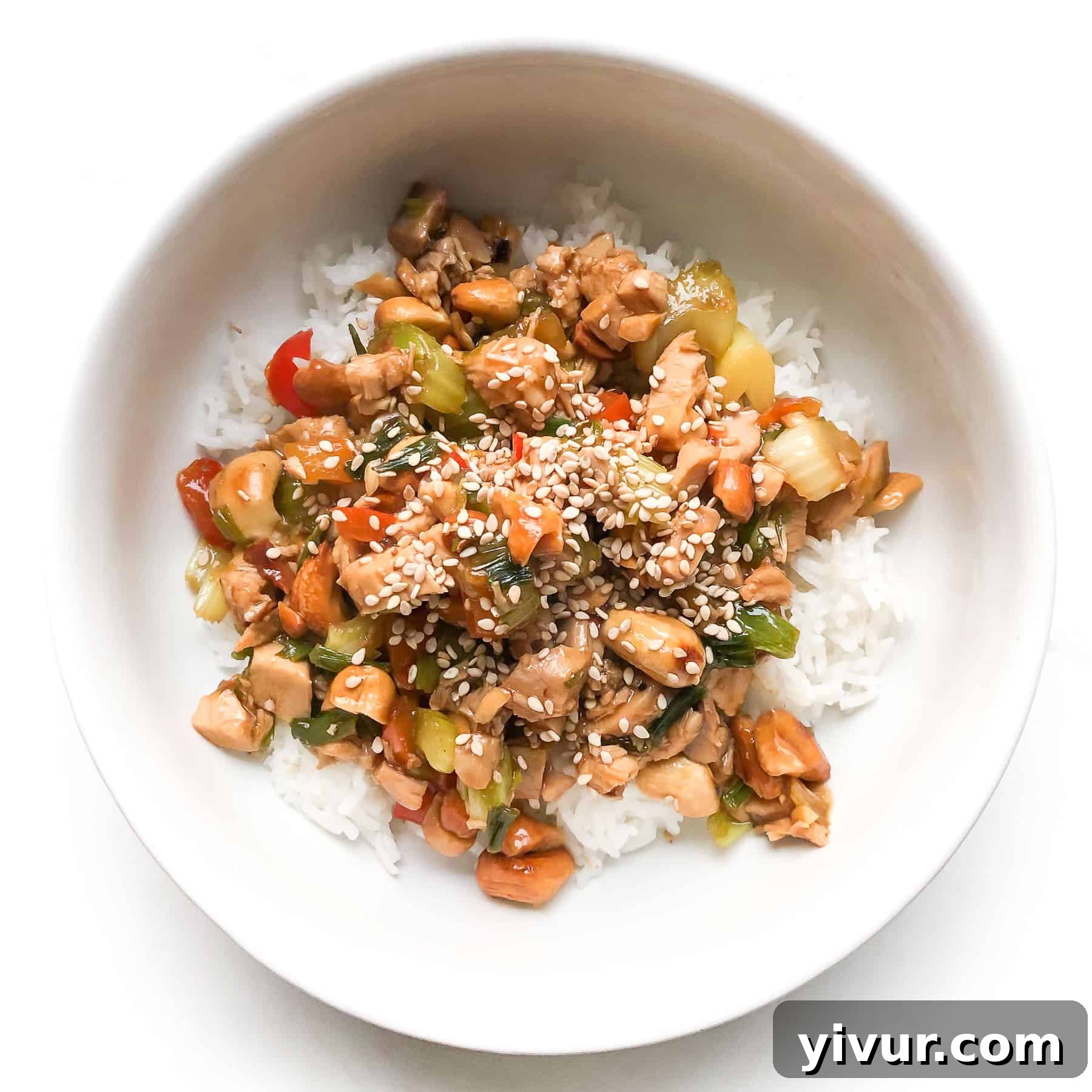 Chicken and celery stir fry in a white bowl topped with sesame seeds over cauliflower rice, presented on a white background.