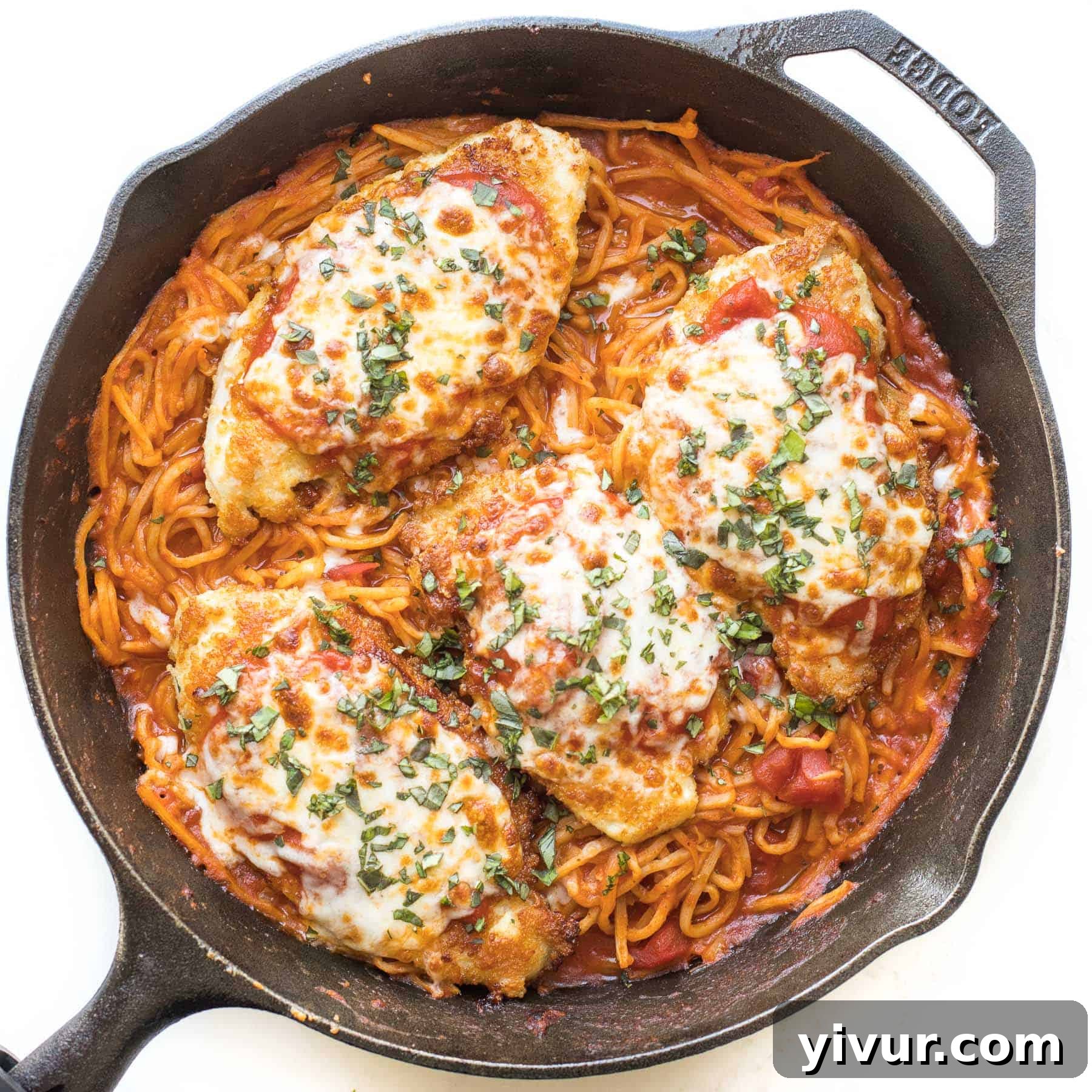 Keto skillet chicken parmesan, bubbling with cheese and sauce, in a cast iron skillet on a white background.