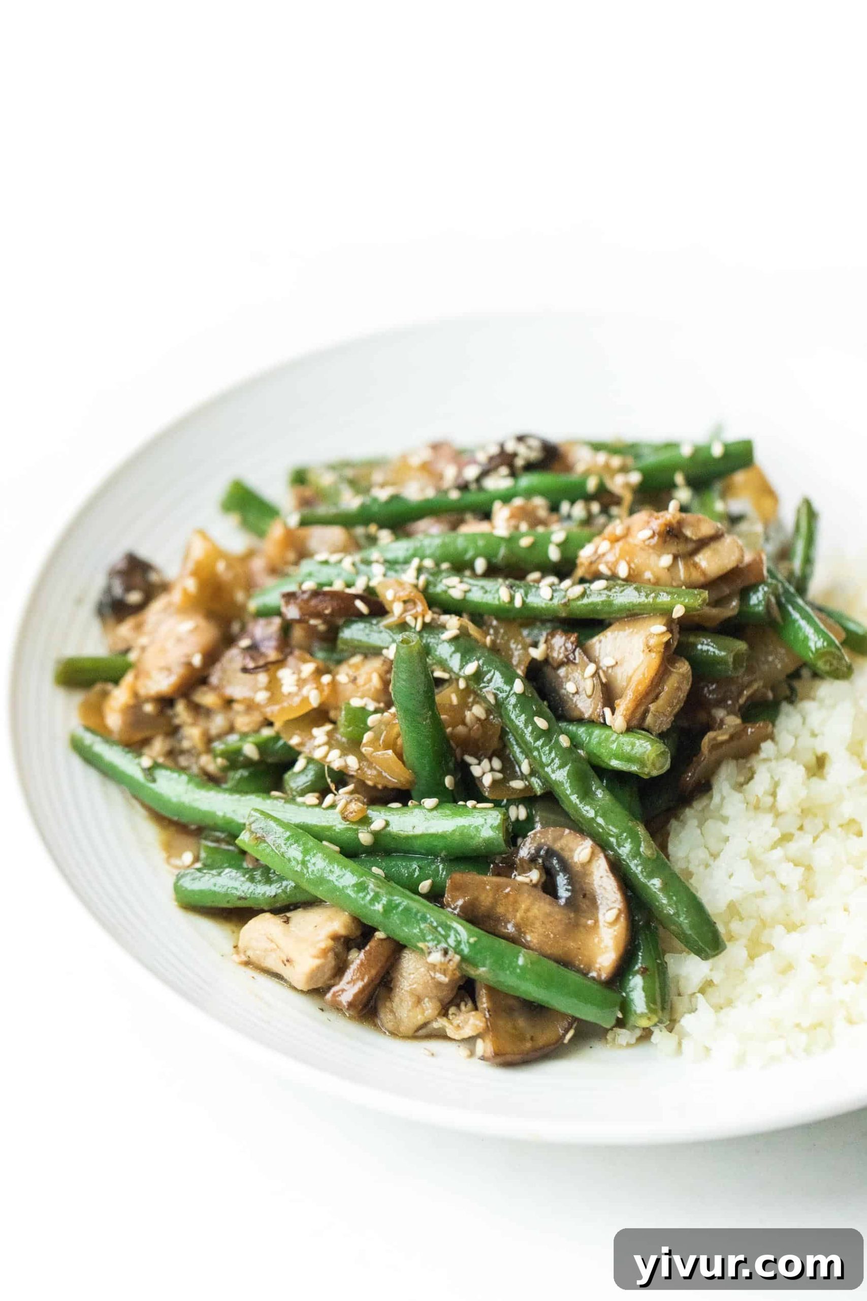 Sesame chicken green bean stir fry on a white plate with cauliflower rice. Paleo + Whole30 Sesame Chicken Green Bean Stir Fry Recipe - a quick and delicious dinner or lunch meal prep! Easy homemade stir fry sauce recipe. Gluten free, grain free, dairy free, refined sugar free, clean eating, real food. #paleo #whole30 #stirfry