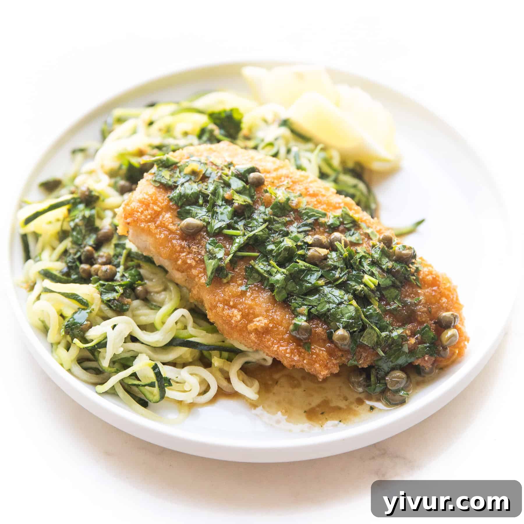 Breaded lemon keto chicken piccata served over zucchini noodles on a white plate and background.