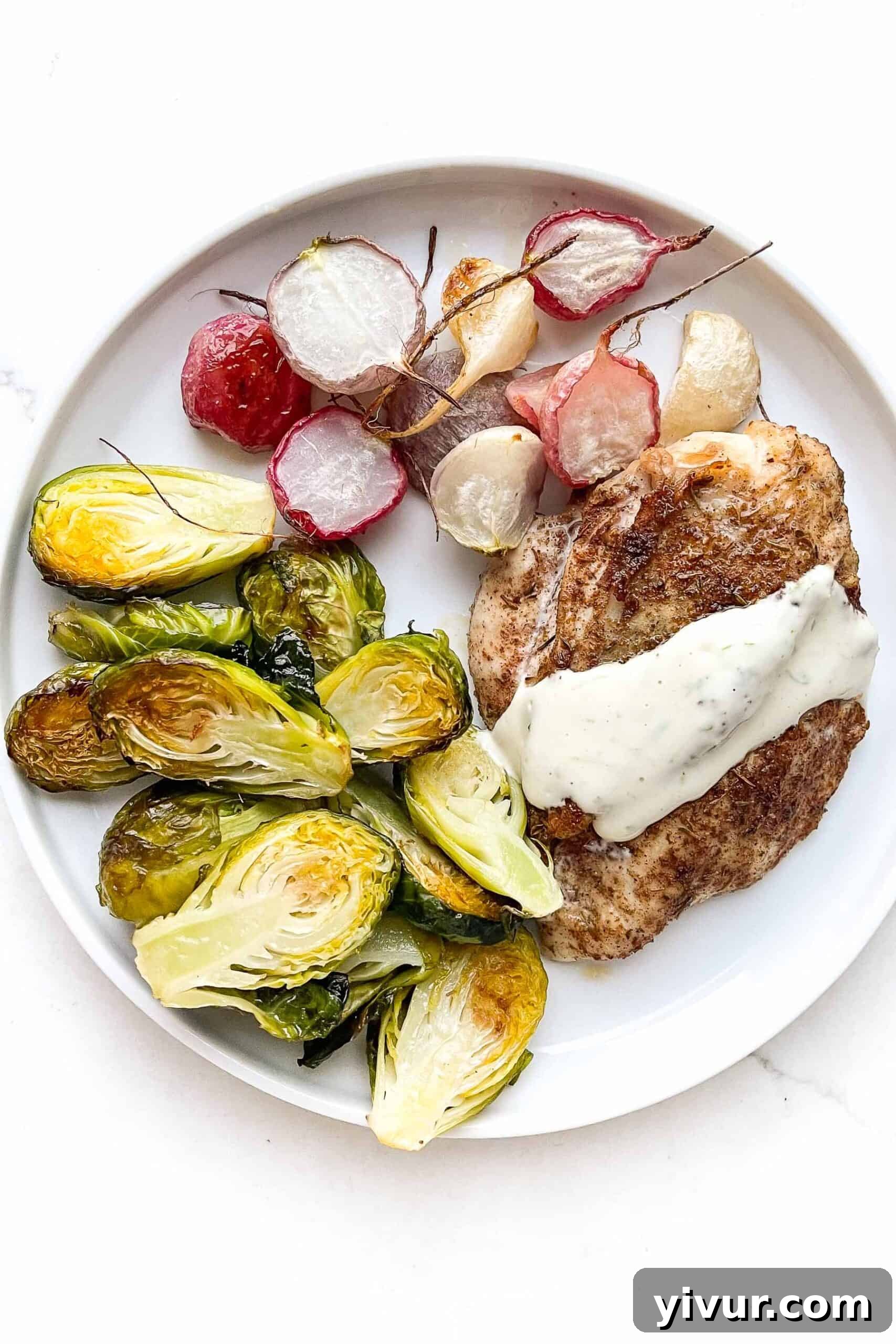 Jerk seasoned chicken breast topped with garlic lime aioli, roasted brussels sprouts, and roasted radishes on a white plate with a white background.