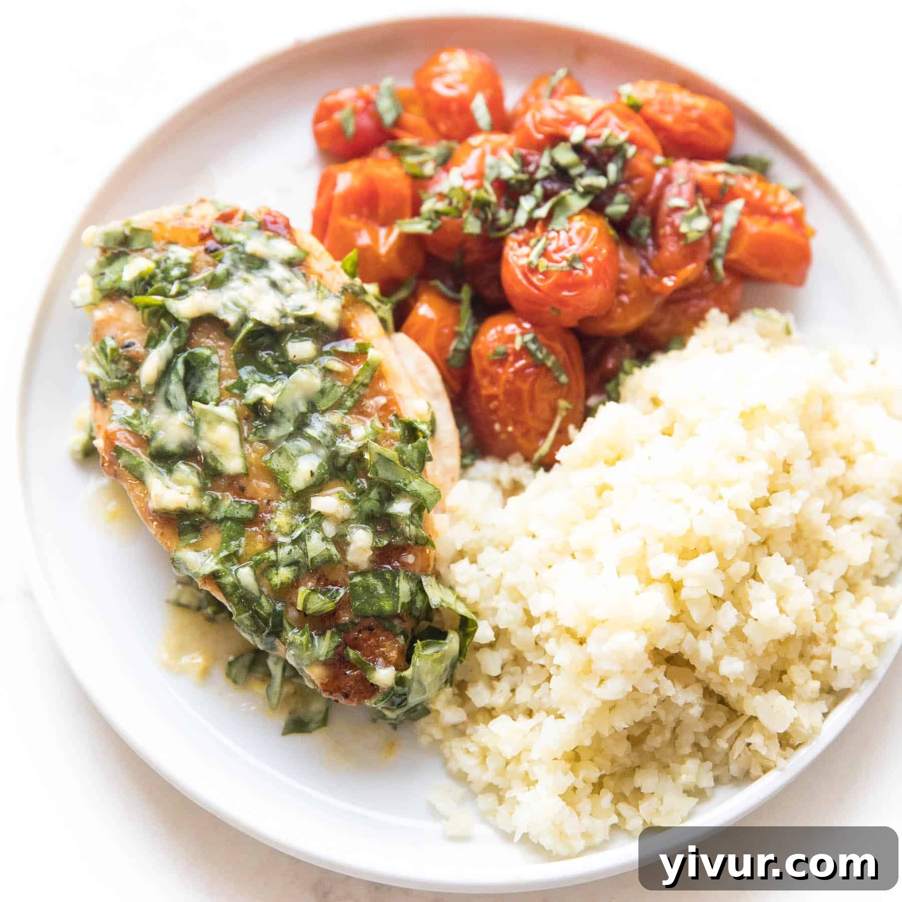 Chicken with basil butter, blistered tomatoes, and cauliflower rice on a white plate, cooked in a skillet.