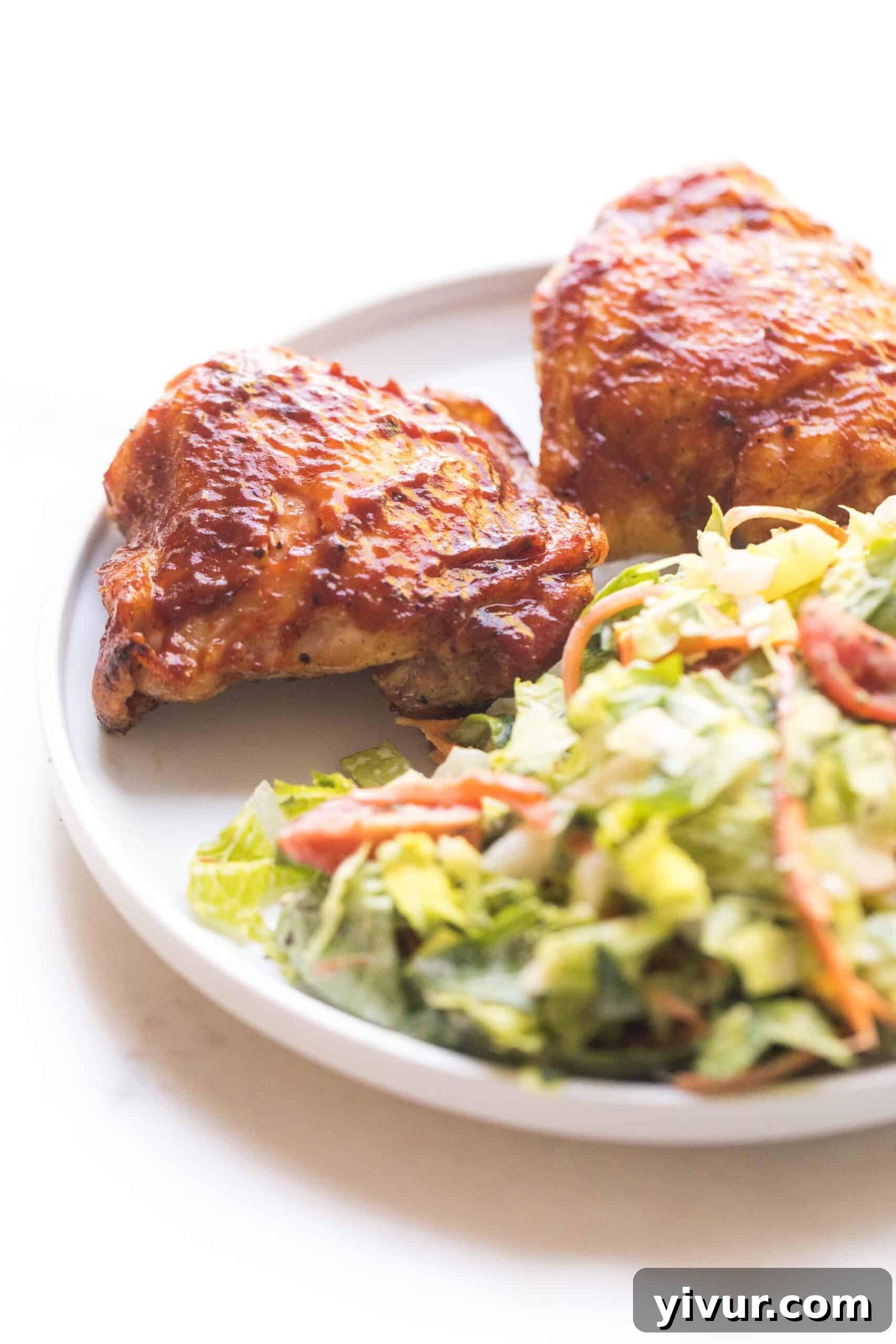 Tender BBQ chicken thighs on a white plate with a fresh green salad, coated in a savory keto-friendly sauce.