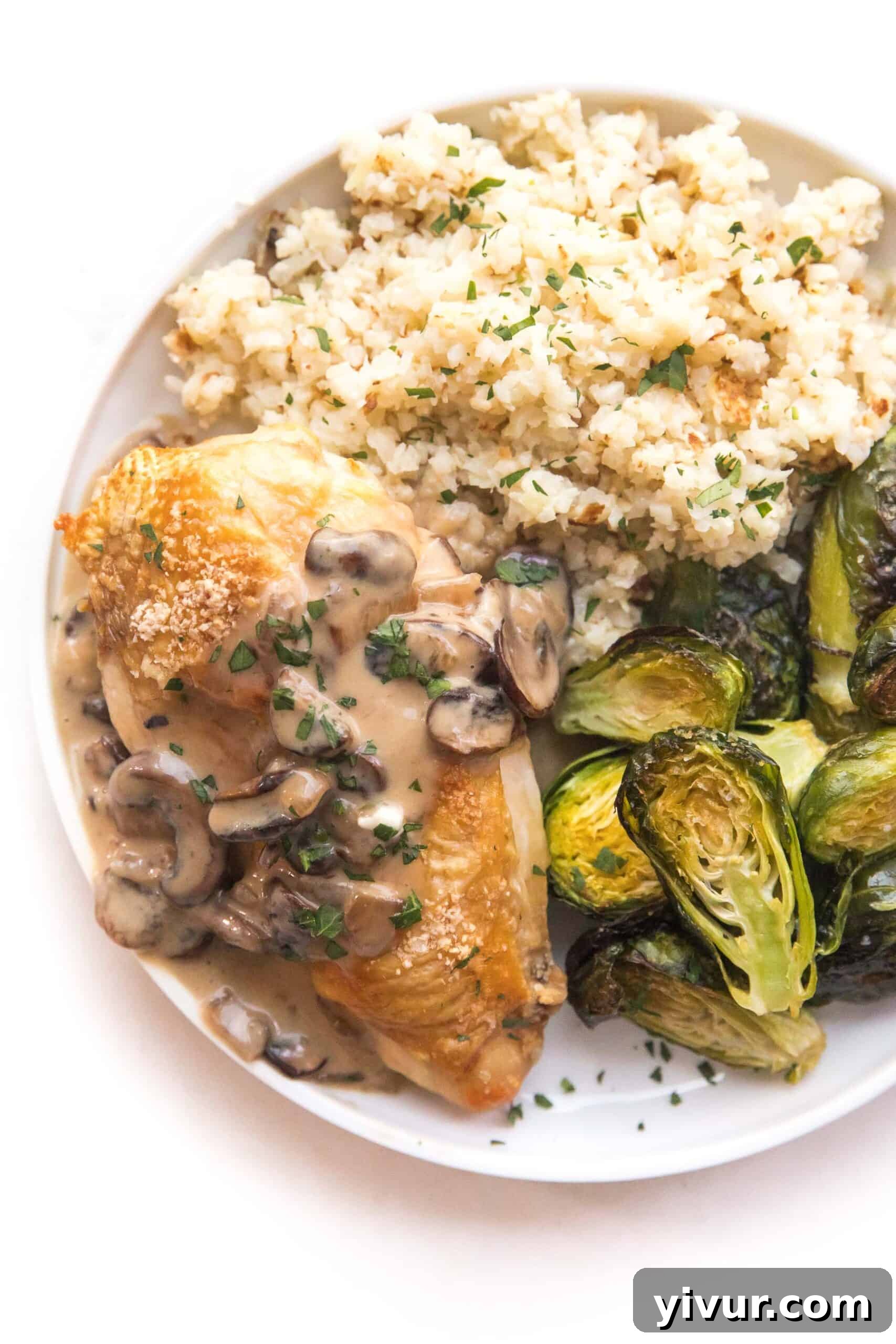 Chicken with creamy mushroom gravy on a white plate and background, served with roasted brussels sprouts and cauliflower rice.