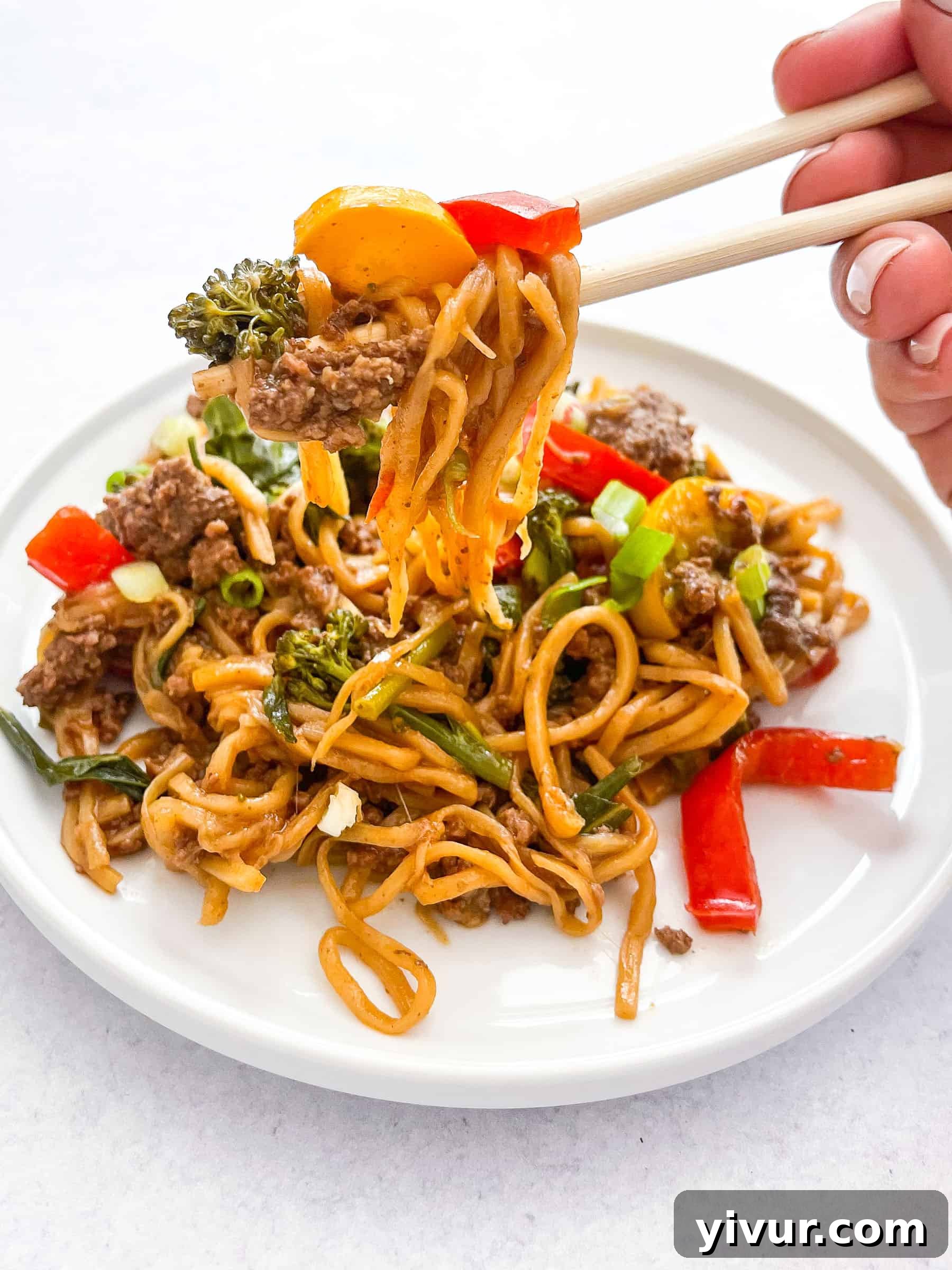 Close-up of keto stir fry with beef and hearts of palm noodles on a white plate, chopsticks lifting a bite