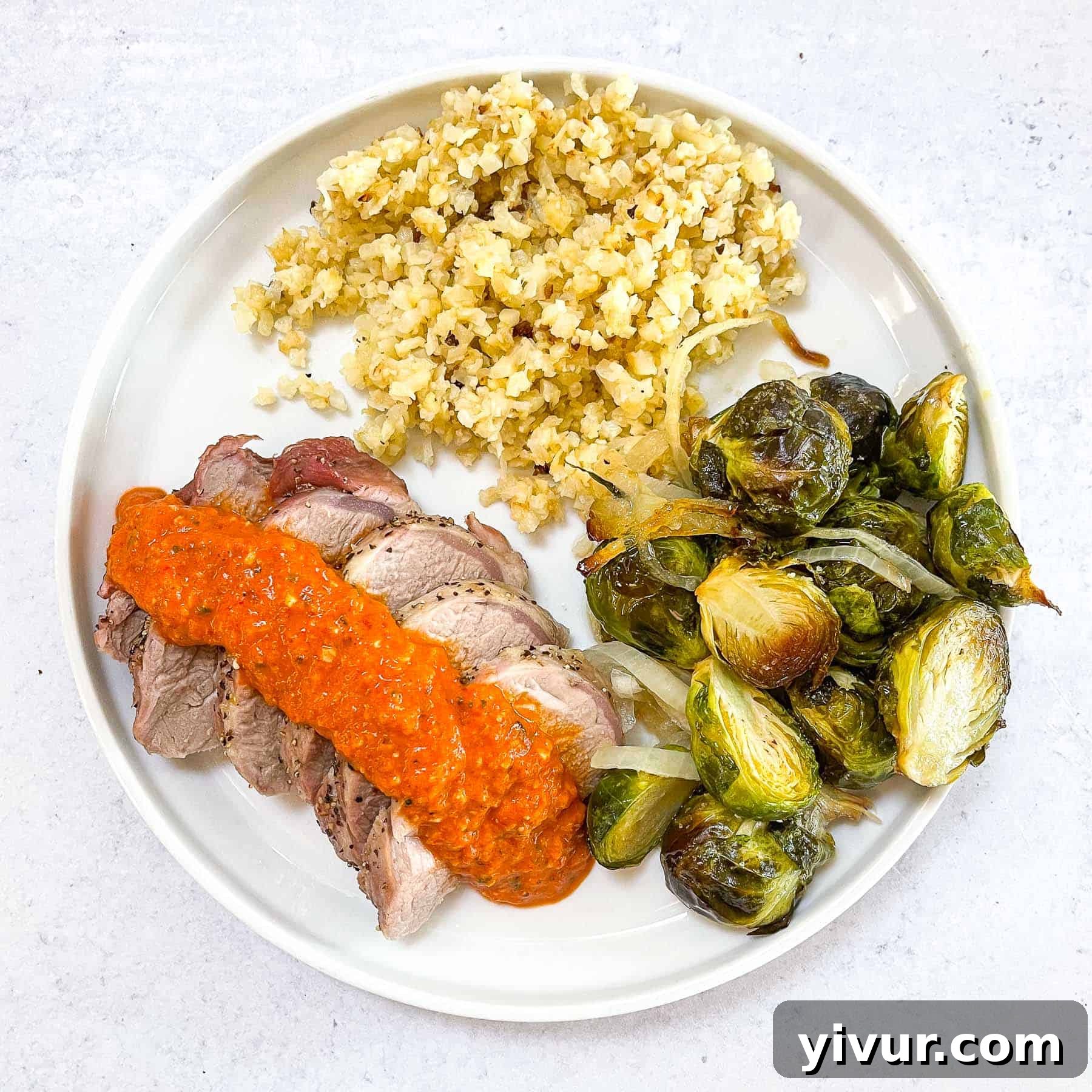 Keto Sheet Pan Pork Tenderloin with Romesco on a white plate, served with roasted Brussels sprouts and cauliflower rice, ready to be enjoyed.