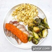 Keto Sheet Pan Pork Tenderloin with Romesco served on a white plate with roasted Brussels sprouts and cauliflower rice.