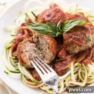 A fork cutting into a tender, juicy Italian meatball made without breadcrumbs.