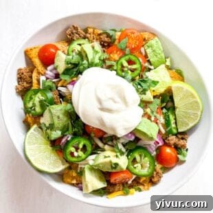 Vibrant keto taco salad with romaine lettuce, seasoned ground beef, tomatoes, cheese, and a dollop of sour cream in a white bowl.