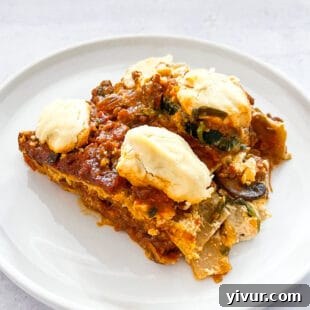 Slice of dairy-free lasagna topped with creamy vegan ricotta cheese on a white plate.