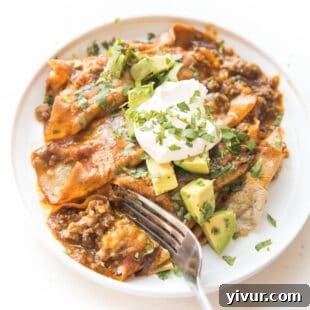 Fork cutting into a bubbling dish of Keto Beef Enchiladas.