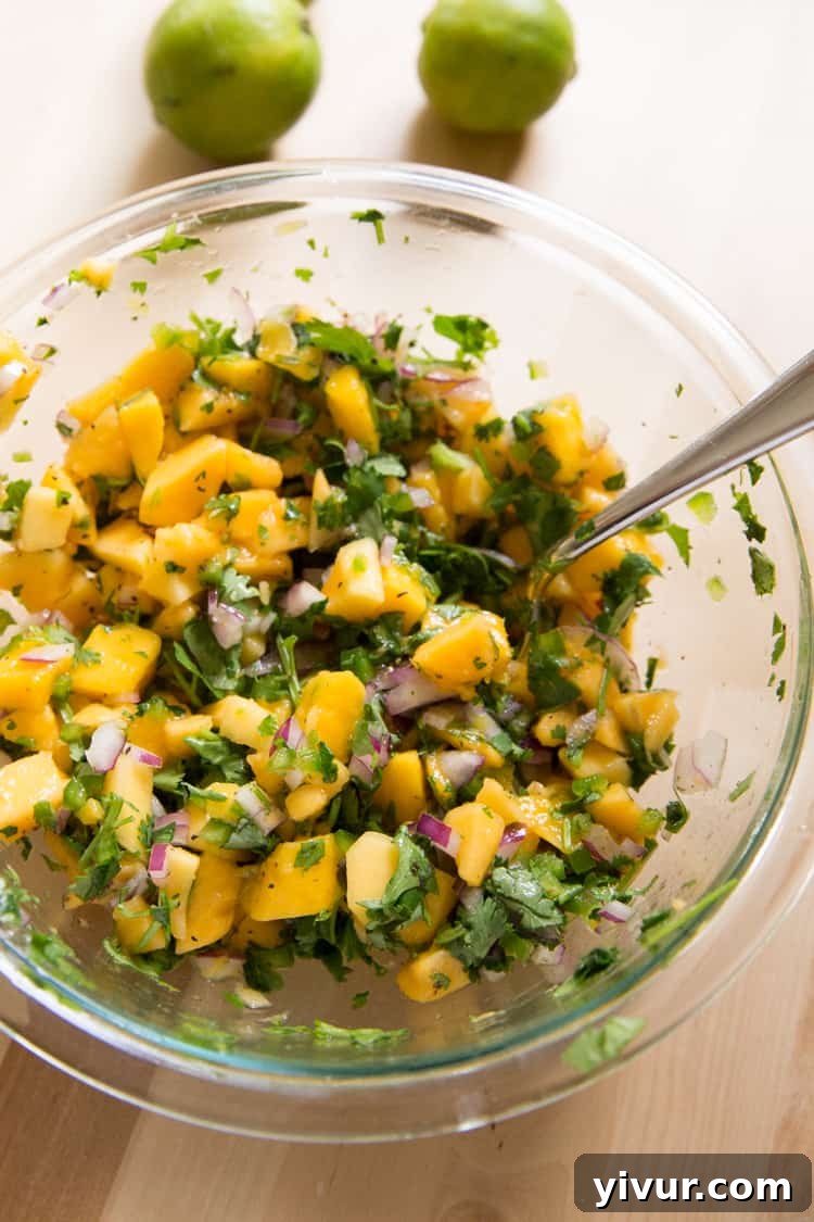 A bowl of mango papaya salsa with a spoon resting inside