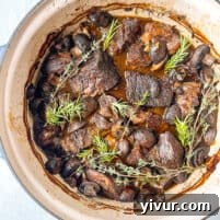 Overhead shot of braised beef recipe in a Dutch oven with fresh herbs as a garnish.
