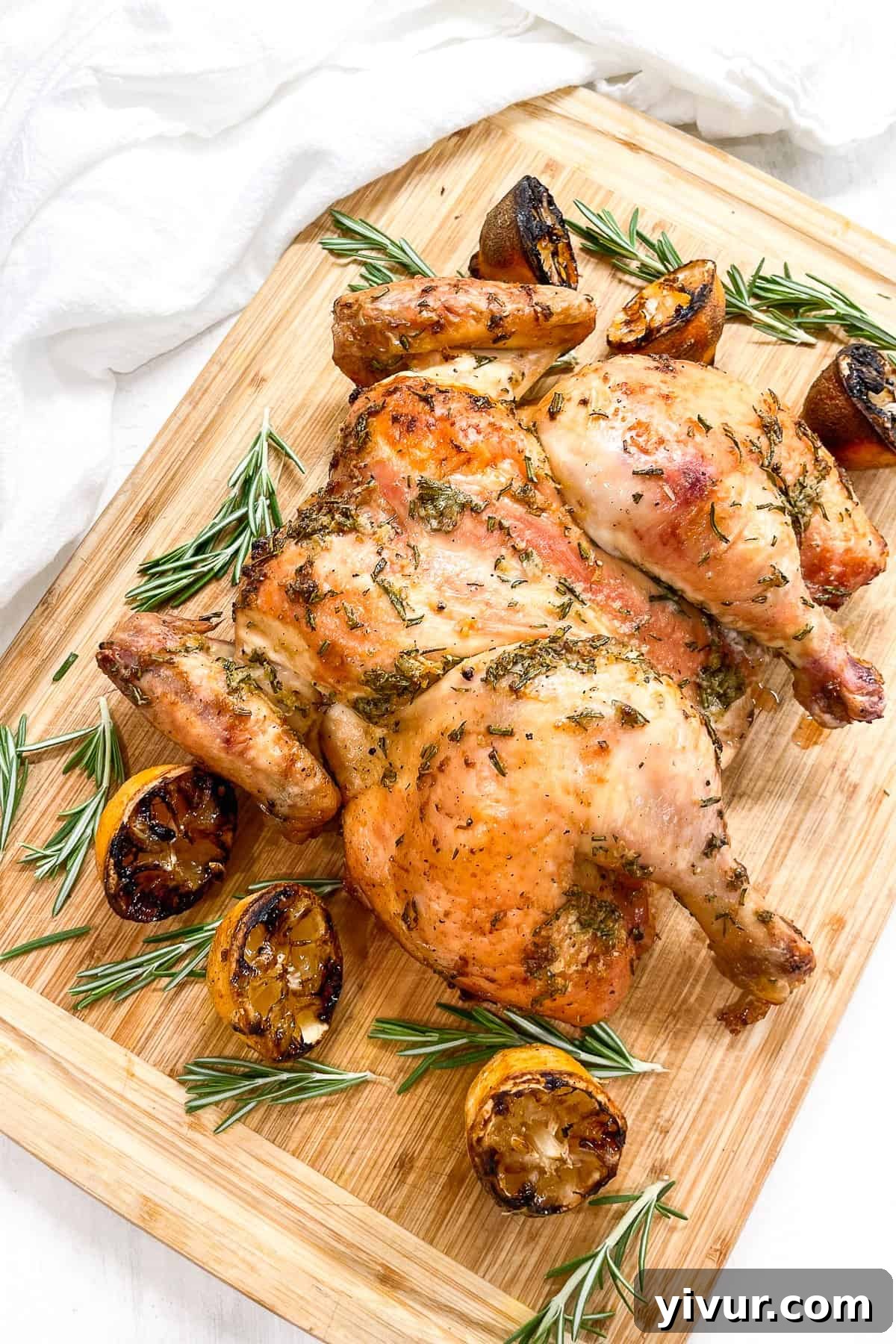 cooked spatchcocked chicken with a rosemary lemon marinade on a cutting board with grilled lemons and fresh rosemary
