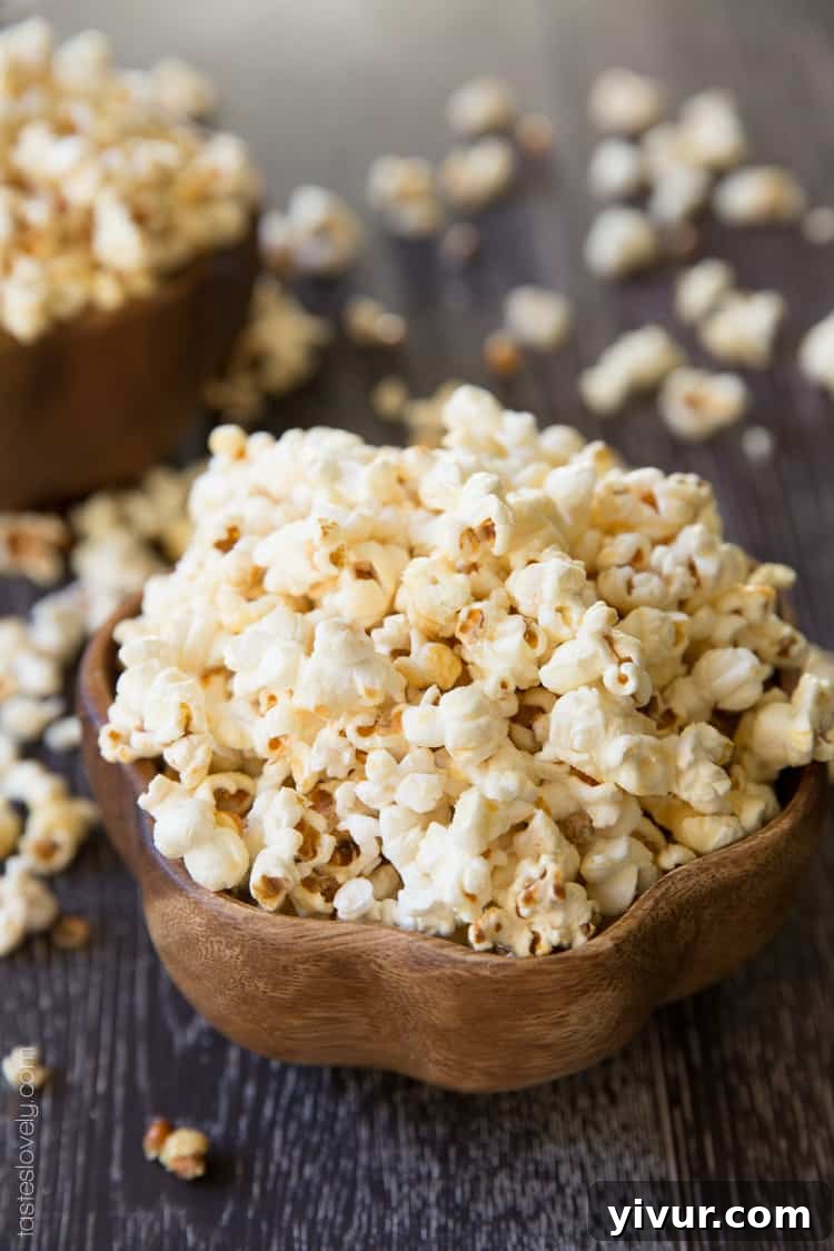 Overhead view of a large bowl filled with freshly popped kettle corn, showing the light, golden sugar coating and scattered popcorn pieces on a white surface.