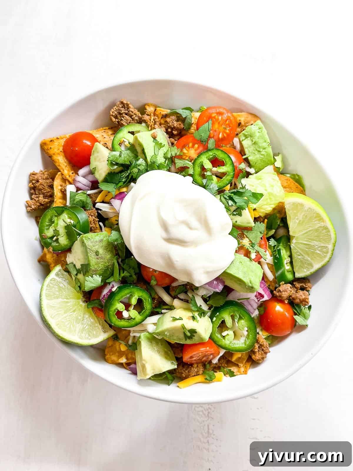 Vibrant keto taco salad with seasoned ground beef, romaine lettuce, cherry tomatoes, cheese, and a dollop of sour cream in a white bowl, garnished with cilantro.