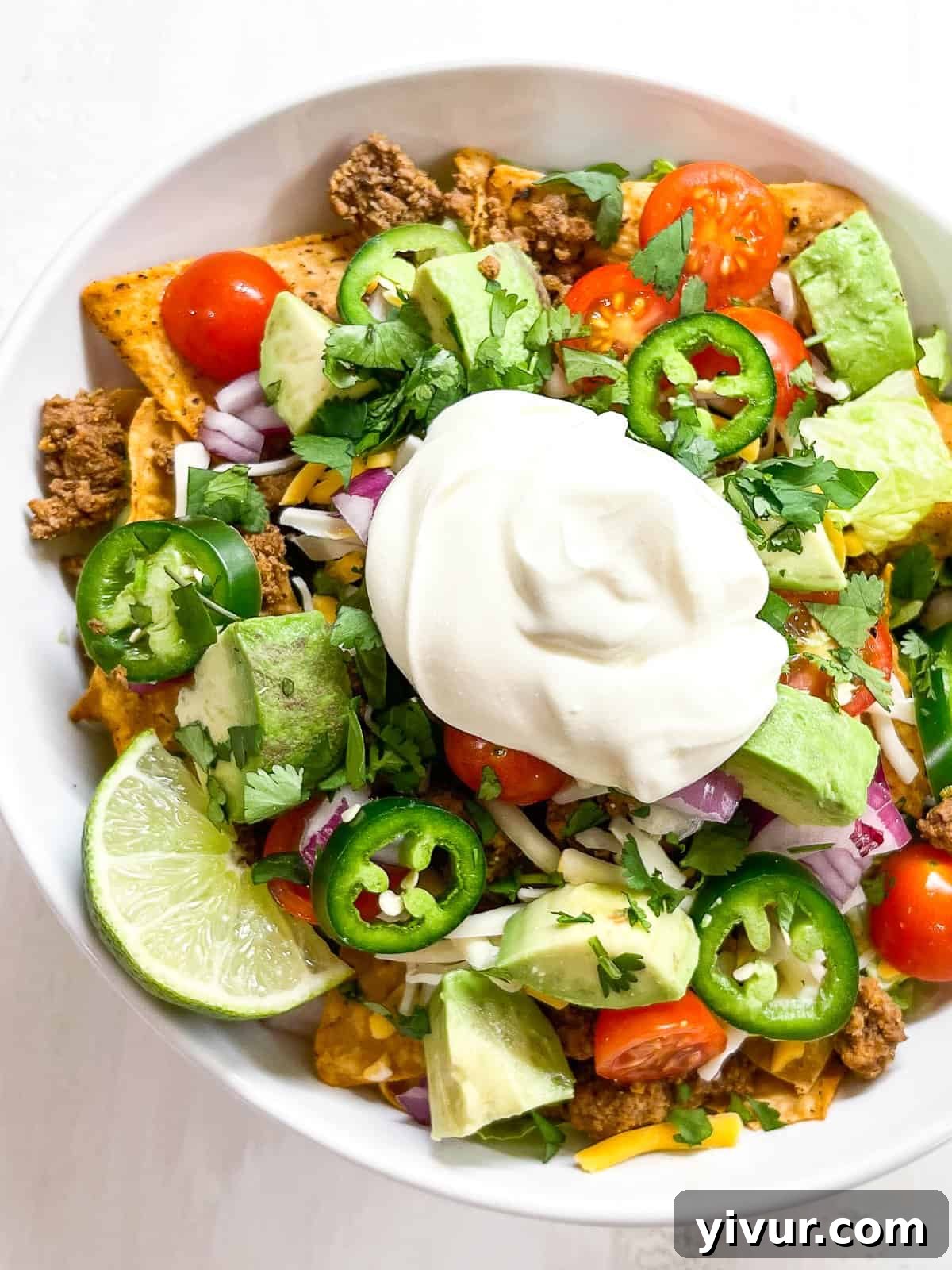 Close-up of a keto taco salad bowl showing the layers of seasoned ground beef, fresh green lettuce, vibrant red tomatoes, shredded cheese, and a dollop of sour cream.