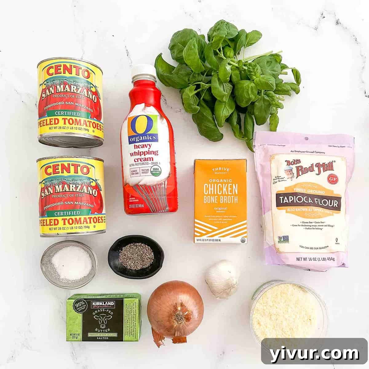 Recipe ingredients laid out on a white surface, including canned tomatoes, fresh basil, butter, garlic, and cheese