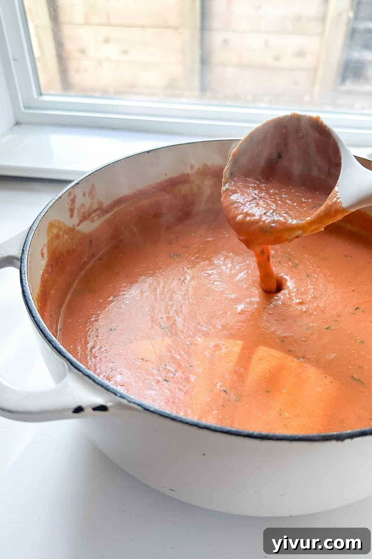 A ladle scooping creamy tomato basil soup out of a pot, highlighting its rich texture
