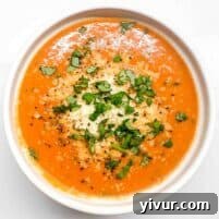 An overhead shot of a white bowl filled with creamy tomato basil soup