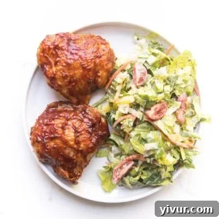 Grilled BBQ chicken thighs served on a white plate, accompanied by a fresh green salad.