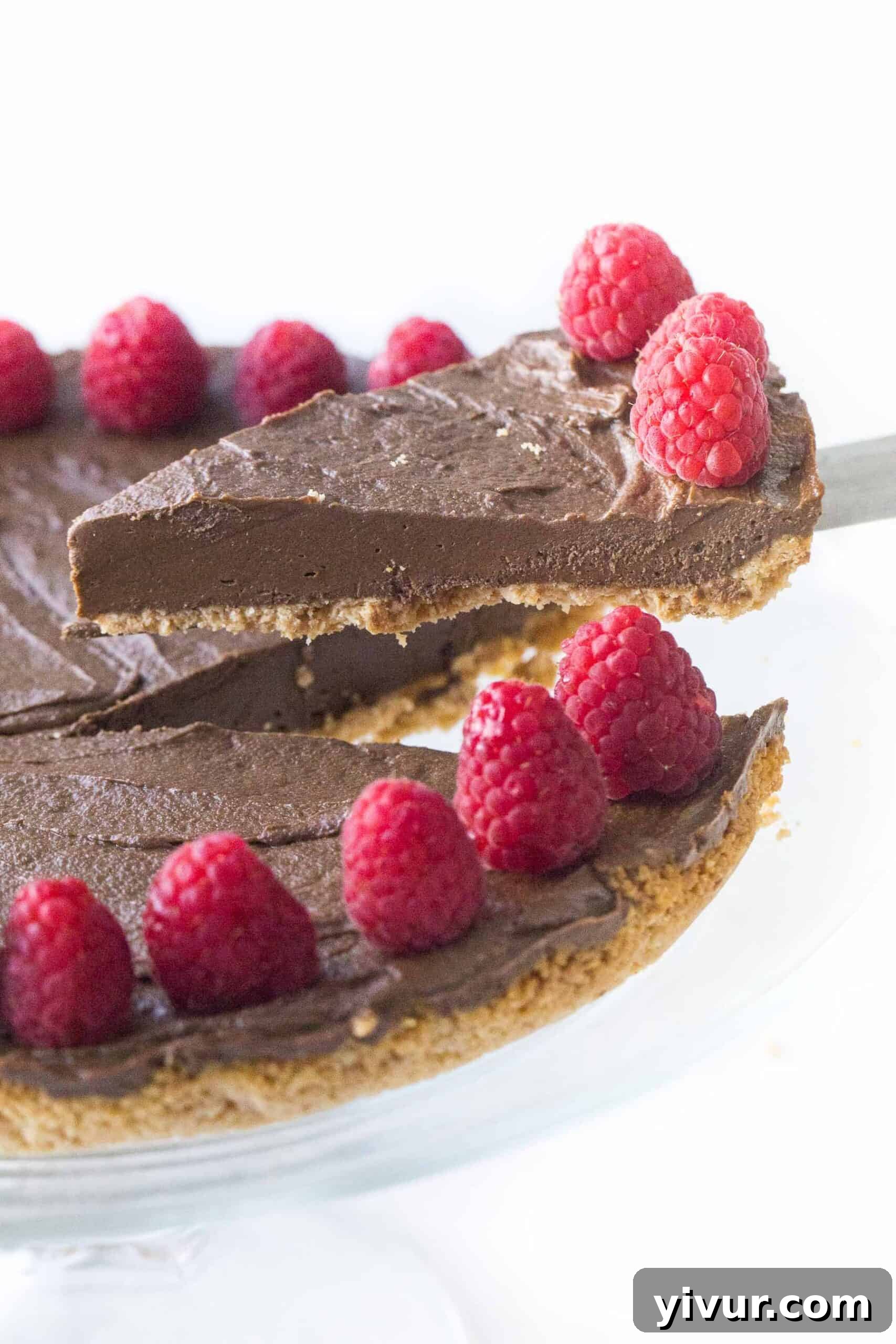 Lifting a slice of healthy chocolate tart adorned with fresh raspberries, showcasing its rich texture and perfect crust.