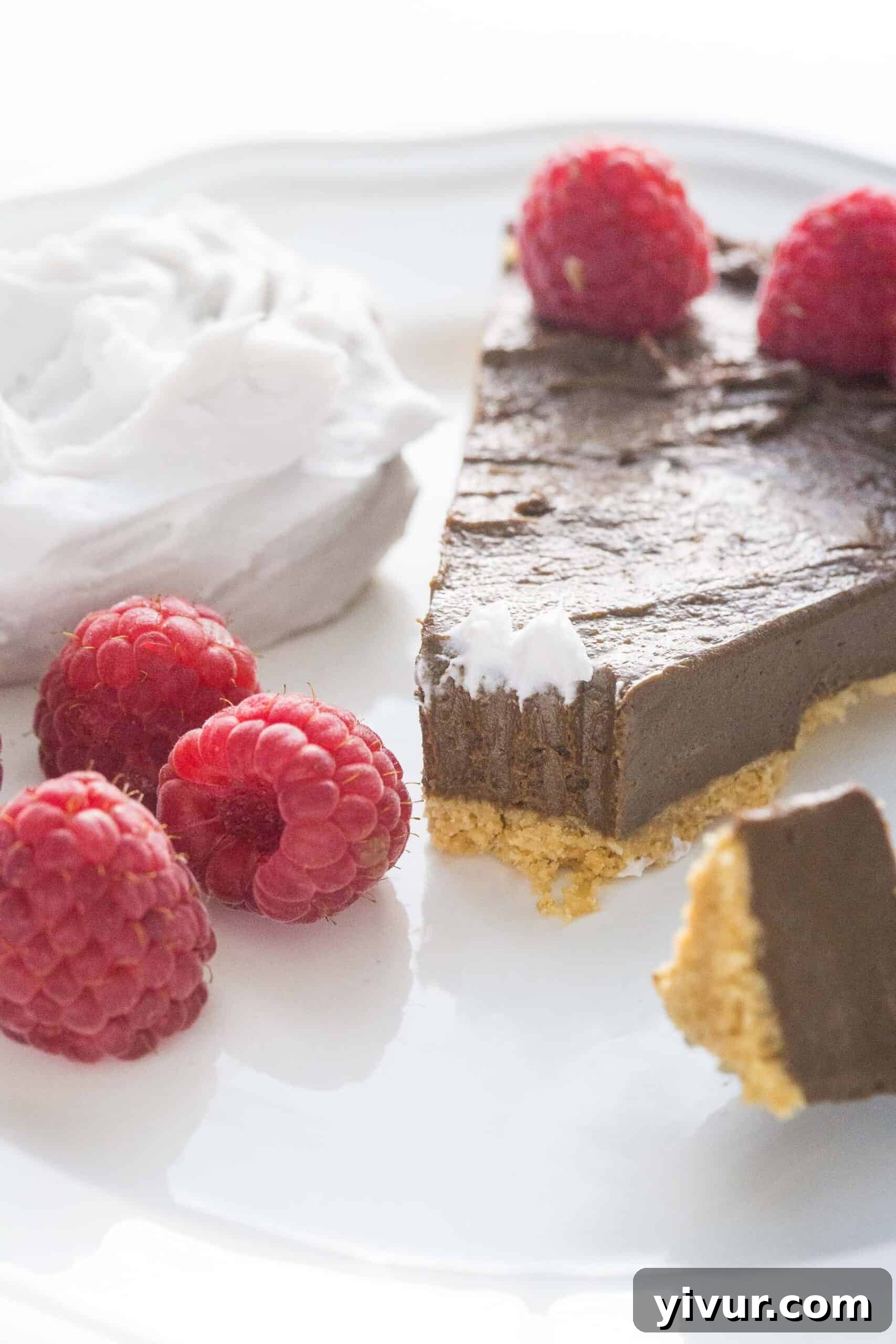 A delectable bite-sized portion removed from a chocolate tart, revealing the rich filling and garnished with fresh raspberries and light coconut whipped cream.