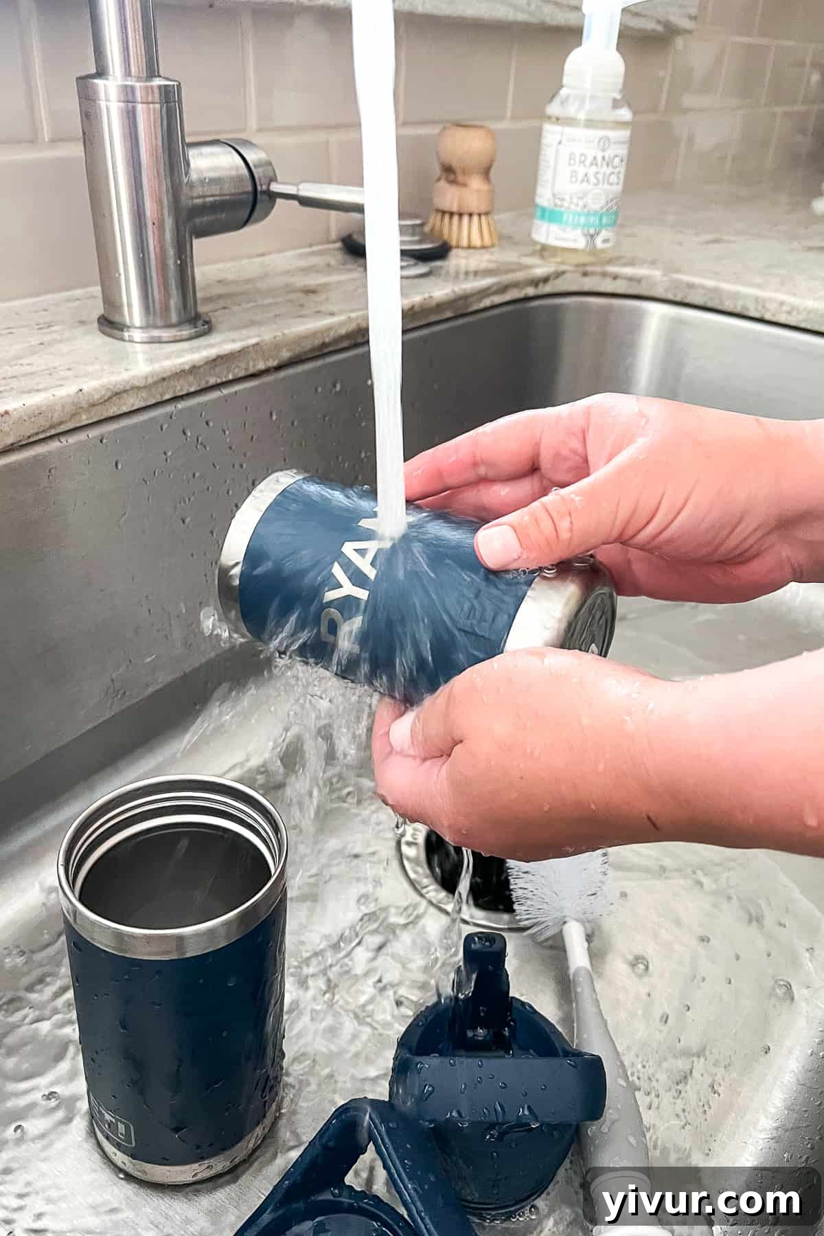 Rinsing freshly cleaned stainless steel water bottles under running water in the sink, washing away all soap residue.