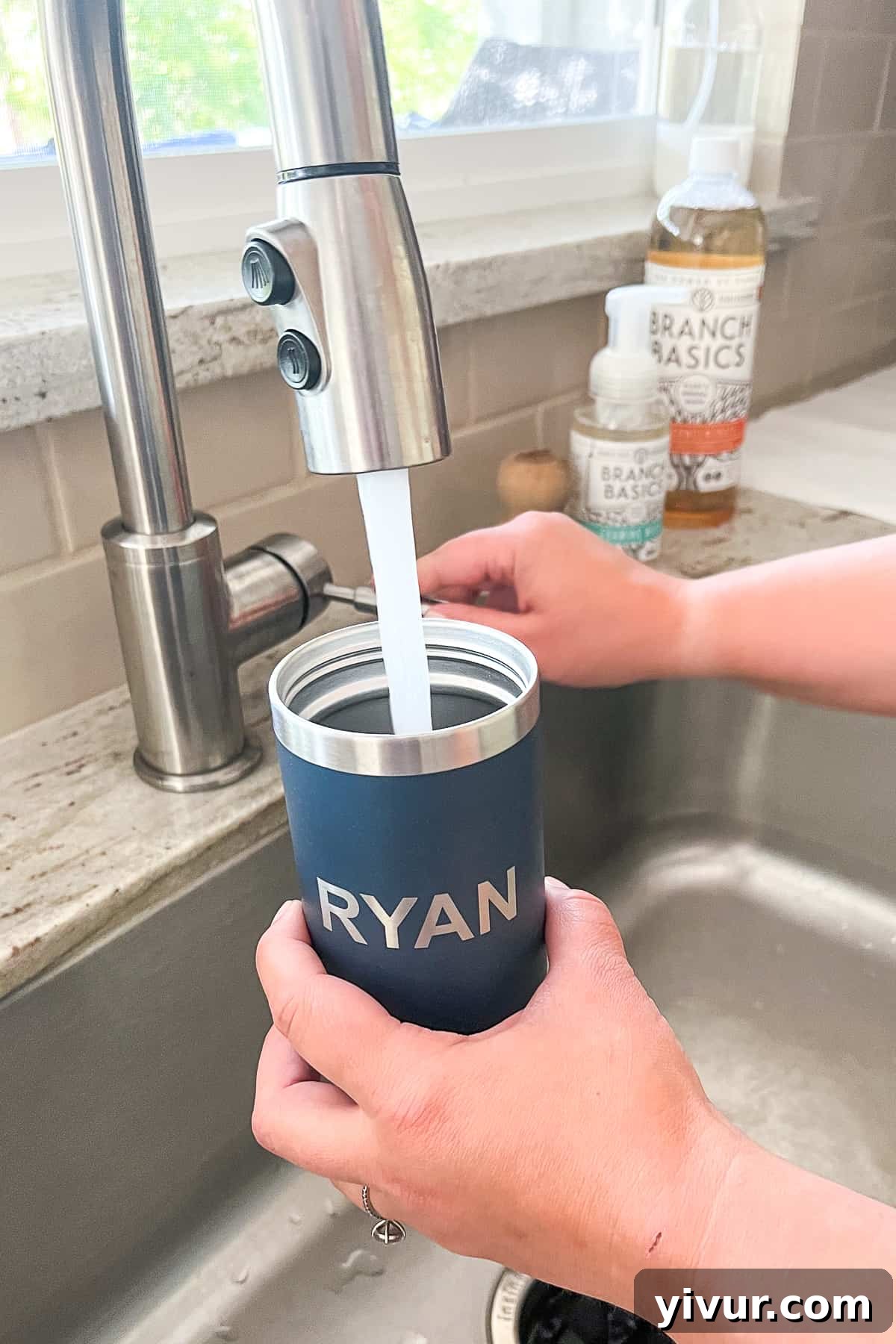A kitchen sink faucet filling a blue stainless steel tumbler with fresh water, ready for hydration after cleaning.
