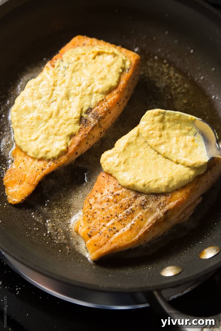 Close-up of crispy Orange Mustard Glazed Salmon fillet on a pan, highlighting its golden-brown crust and vibrant glaze.