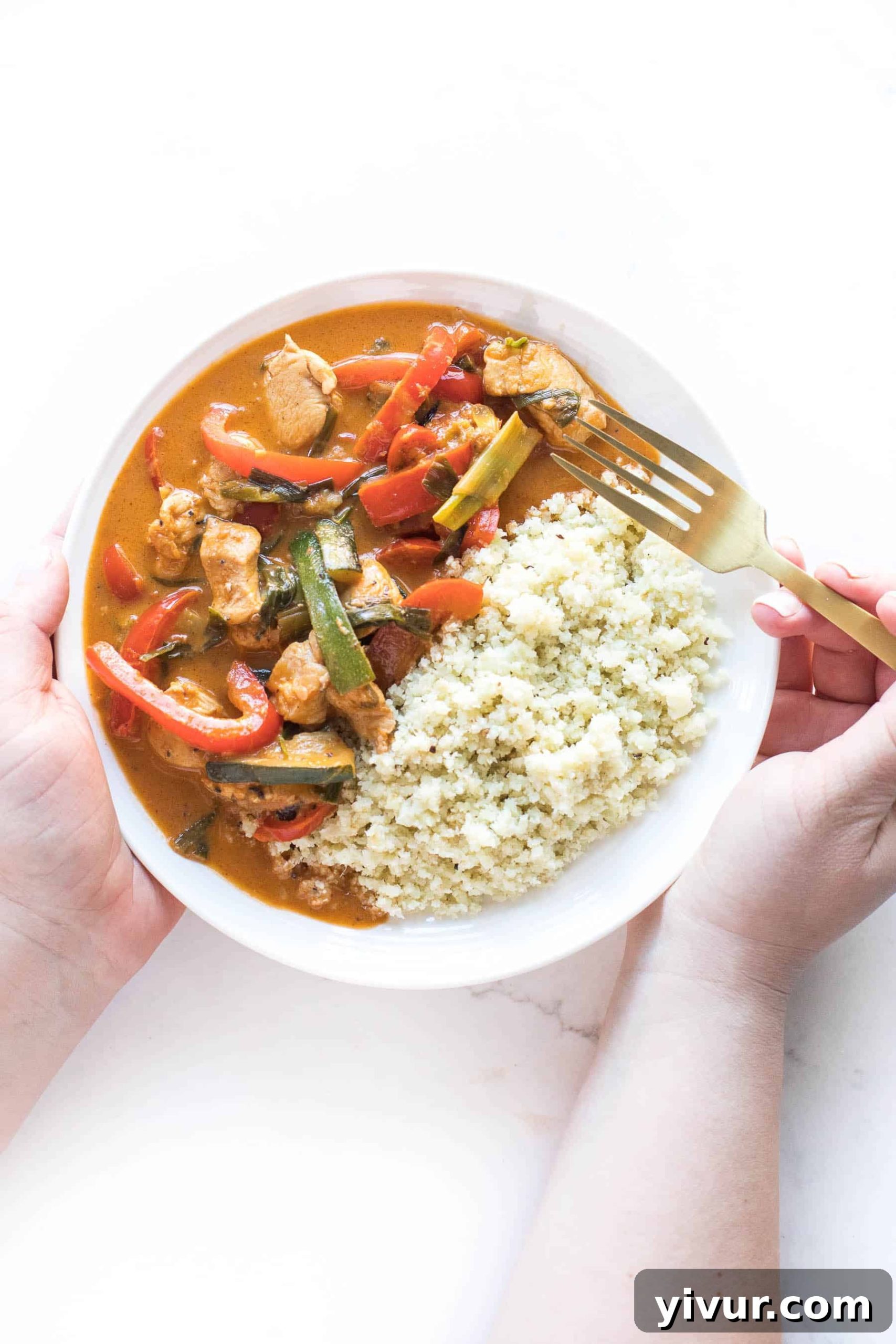 30-Minute Keto Thai Coconut Chicken Curry 5 Two hands holding a plate of keto chicken curry served with cauliflower rice.