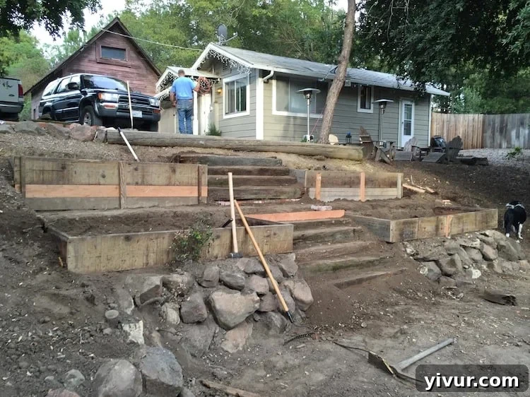 Panoramic view of the terraced garden from the bottom of the hill, showing a large boulder retaining wall and a distant small house