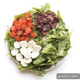 keto salad with bacon, tomatoes and mozzarella cheese on spinach and arugula on a white plate