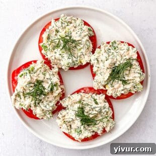 Tuna salad topped with dill on sliced tomatoes on a white plate