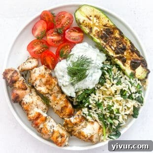 keto grilled chicken kabobs on a white plate with veggies and tzatziki sauce with a white background