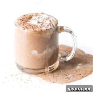 A clear mug of low-carb hot cocoa, topped with a generous swirl of whipped cream and a sprinkle of cocoa.
