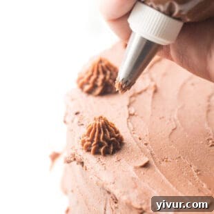 A skilled hand piping rich keto mint chocolate buttercream frosting onto a beautifully baked cake, creating elegant swirls.