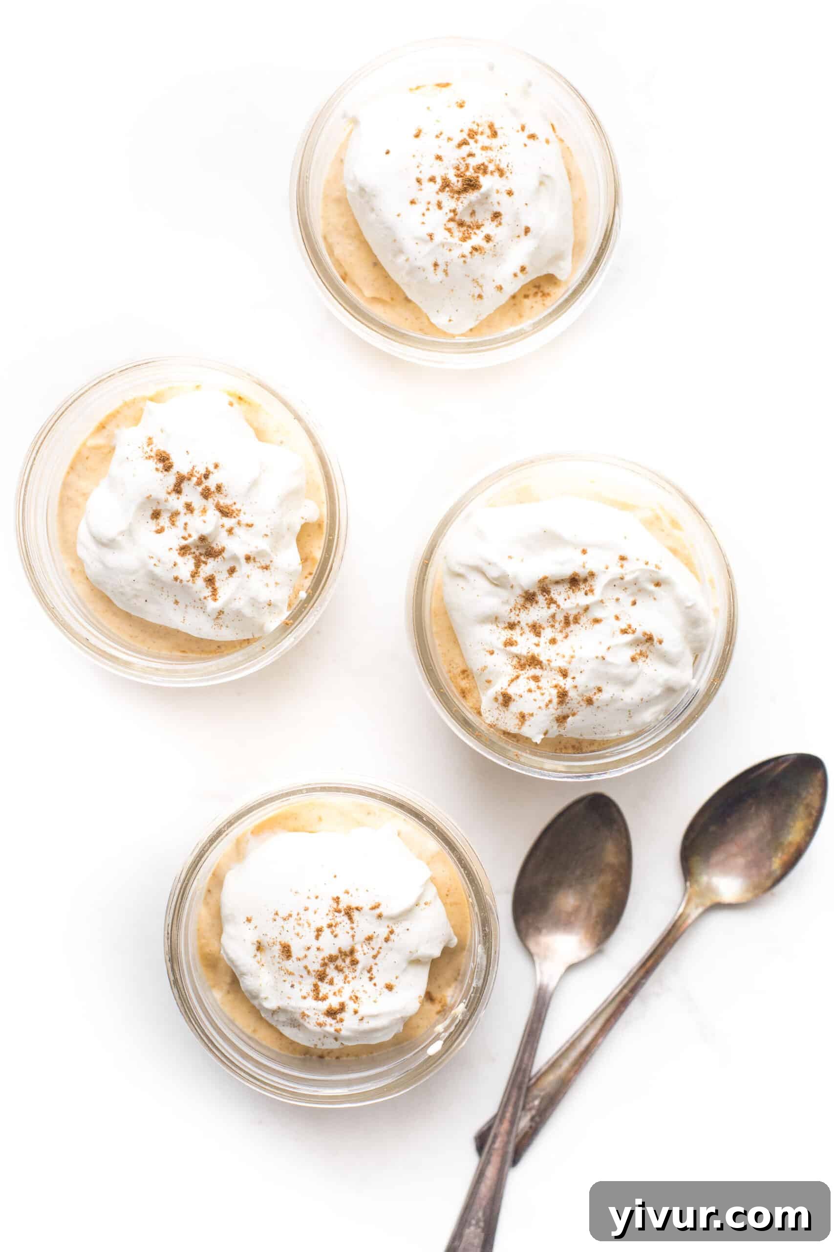 Beautifully layered keto pumpkin cheesecake jars on a white countertop, garnished with a sprinkle of spice.