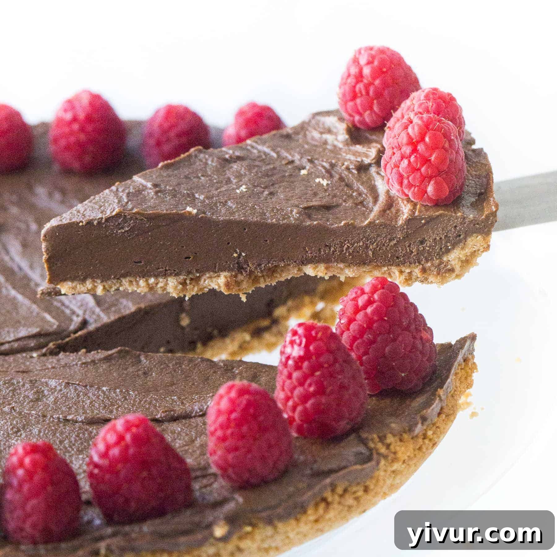A hand lifting a slice of rich, dark healthy chocolate tart, revealing its dense, creamy filling and elegant crust.