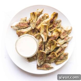 Roasted artichokes on a white plate with a white dip on a white background