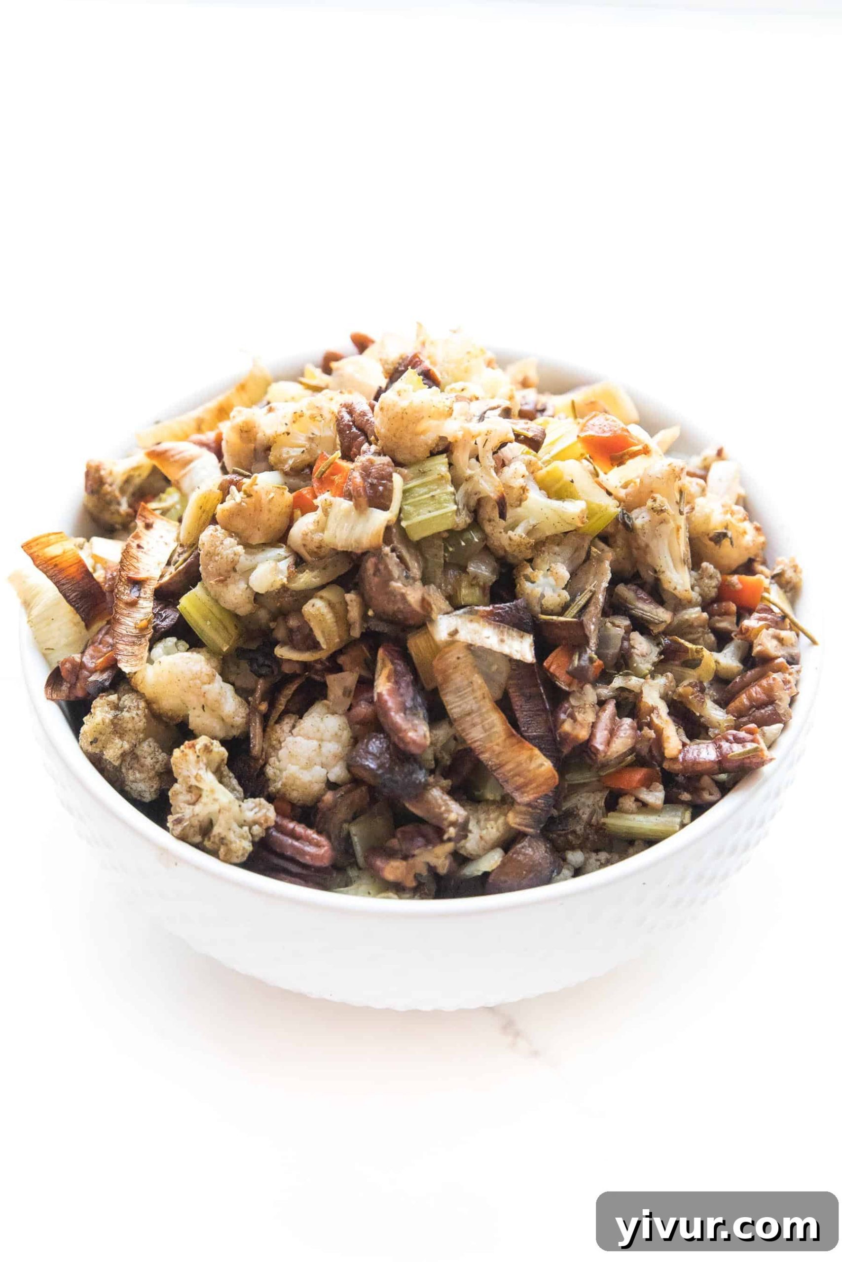 Whole30 + keto cauliflower stuffing in a small white bowl, garnished with fresh herbs.