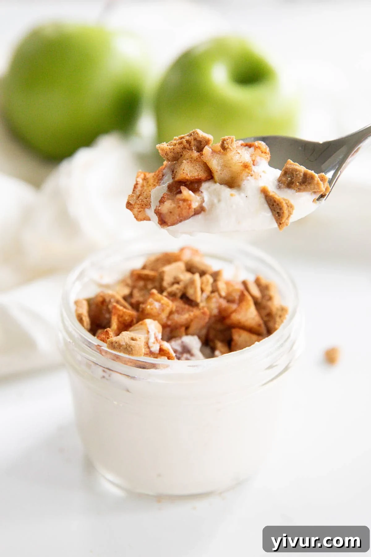 A spoon scooping out cottage cheese cheesecake topped with baked apples and cinnamon from a small mason jar