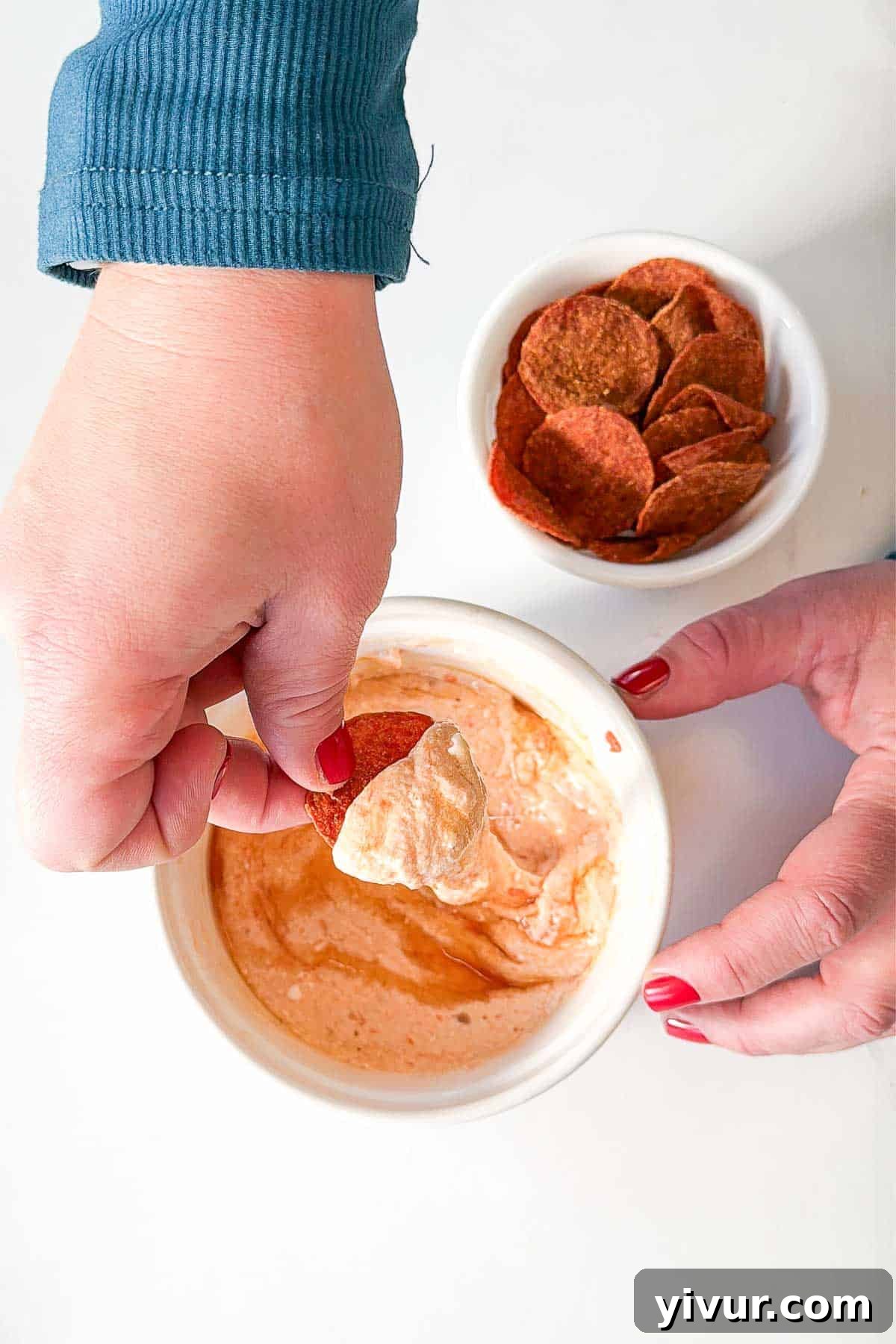 Hand dipping a crispy pepperoni chip into a high protein cottage cheese pizza dip.