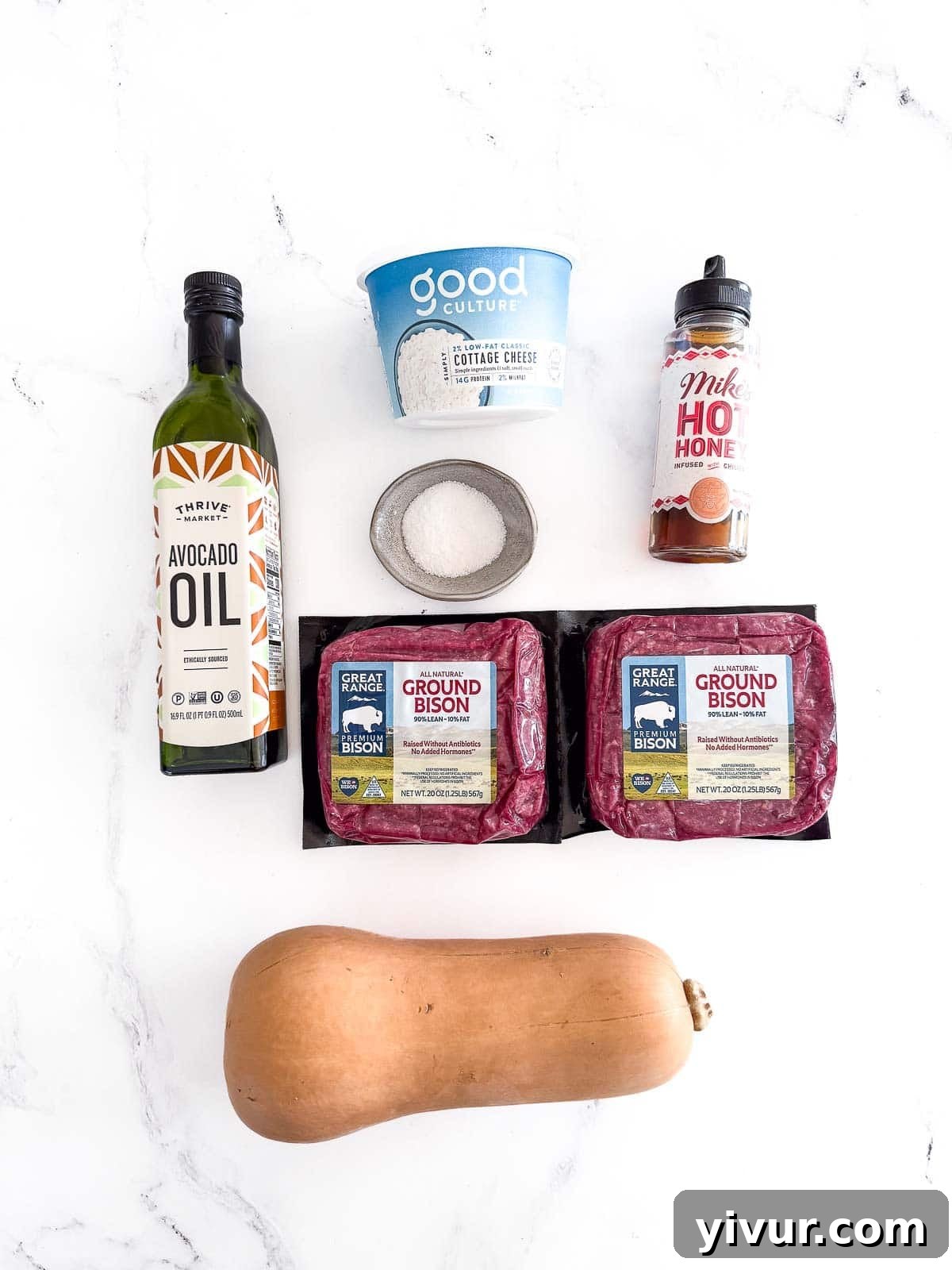 A selection of fresh ingredients including a whole butternut squash, package of ground bison, container of cottage cheese, and a bottle of hot honey, laid out for the High Protein Bison Bowl recipe.